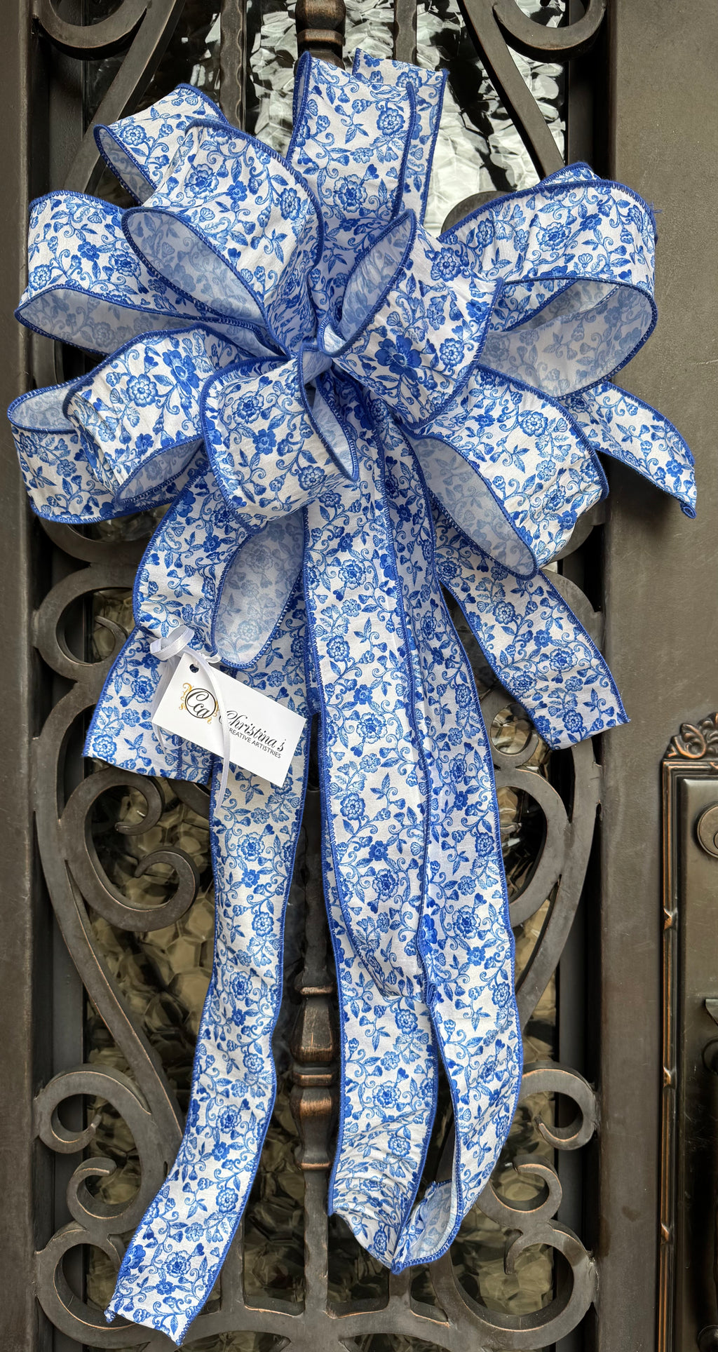 Large BlueWhite Bow product image features a wreath bow. Wired.  Color is blue and white.  Floral pattern.  Measures 19"W X 36"L.  Comes ready to attach to a wreath.  Indoor or outdoor under an overhang.