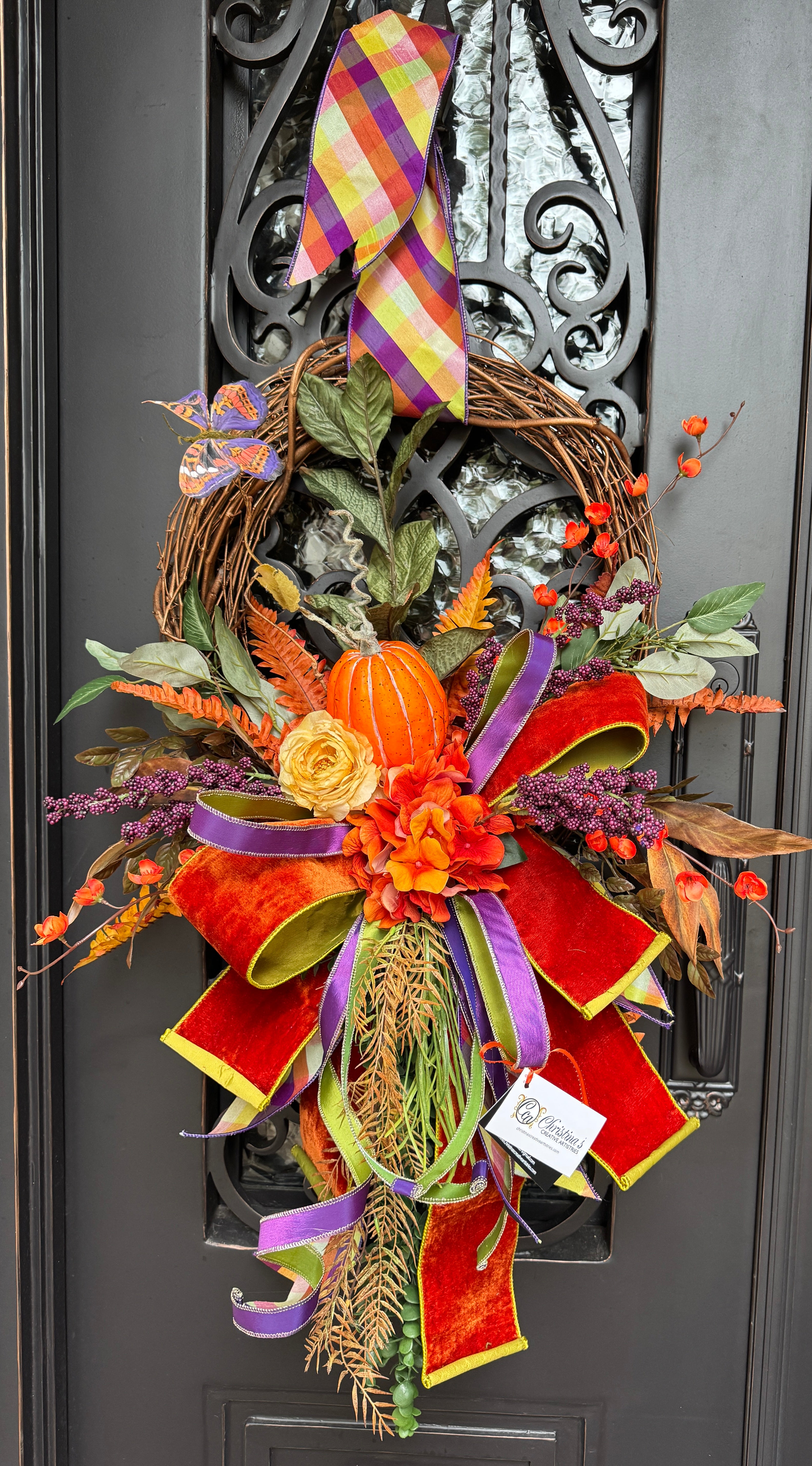 Autumn Wreath with a pumpkin, flowers , mixed greenery, and a beautiful hand tied bow in shades of orange, purple and a hint of yellow.