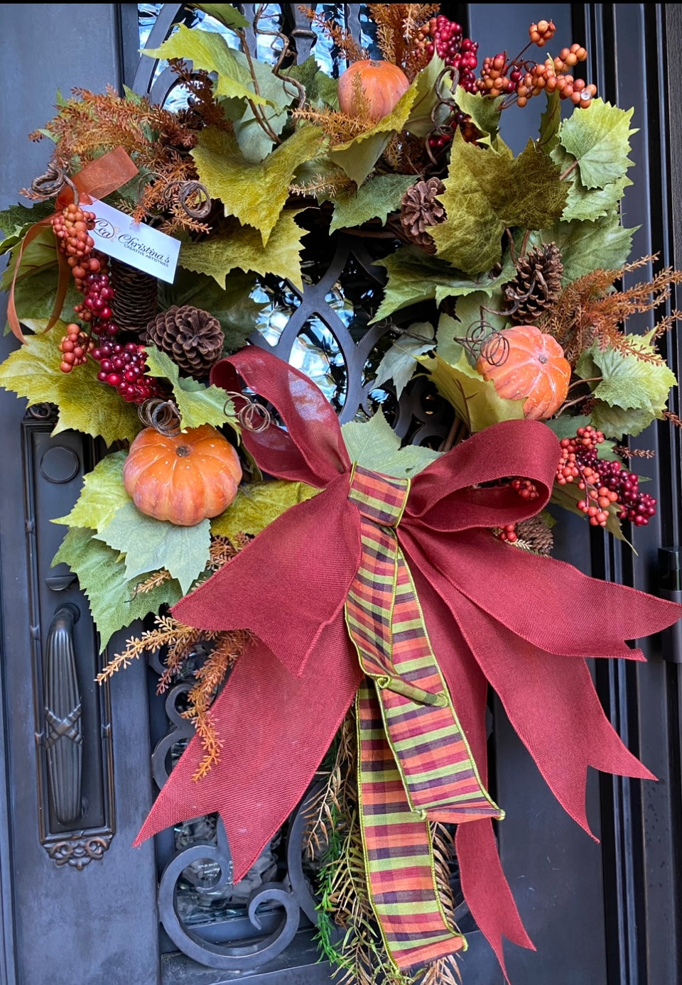   Pumpkins & Berries Fall Wreath product image features a door wreath.  Season is fall.  Materials are faux pumpkins, berries , natural pine cones, pumpkin leaves and a large bow.  Colors are  orange, brown, burnt orange and green.  Measures 40"H X 27" W.  Handcrafted.  Right bow.   Comes ready to hang. 