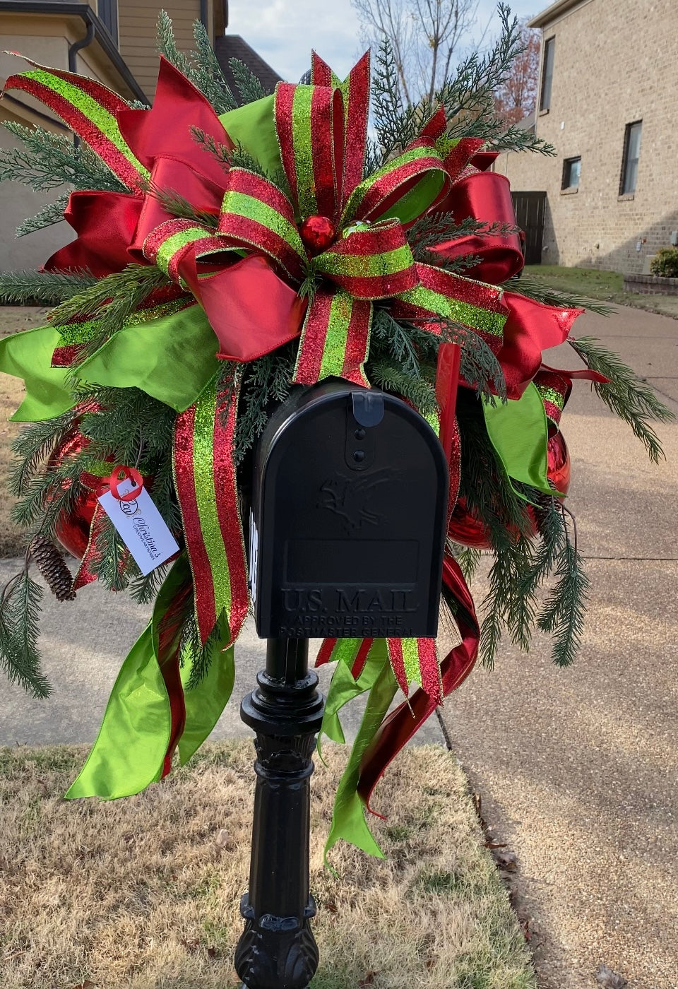Red Green Mailbox Swag product image features a Christmas mailbox swag. Colors are red and green. Mixed pine base, two large ornaments, huge hand tied bow. One glittered ribbon.  Outdoor mailbox use.  Measures 15"H x 20" L x 36"W.