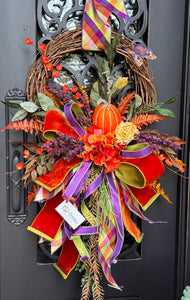 Autumn Wreath with a pumpkin, flowers , mixed greenery, and a beautiful hand tied bow in shades of orange, purple and a hint of yellow.