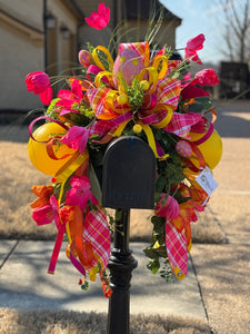 Easter Mailbox Decoration product image features a mailbox swag.  Layers of ribbons, faux tulips, faux eggs, large ball ornaments, mixed greenery.  Colors are pinks, yellow and orange.  measures 40"h x 40" W x 23" L.  Slides right onto mailbox.