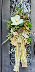 Fall Magnolia Swag product image features a beautiful fall door swag.  A large magnolia, one large, natural twig grapevine ball, one white gourd, artificial feathers, and berries with mixed greenery and a large, double bow.  Colors are cream, natural and green.  Hanging measurements are 46"L x 24"W X 12" D.  Comes ready to hang. 