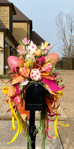 Easter Mailbox Swag product image features a mailbox swag. Hand painted eggs , rabbit hats, mixed greenery and a mix of 5 different wired ribbons. Colors are pink, yellow, orange, white and green. Wired ribbons. Measures 45"H x 28" W x 24"L. Slides right onto your mailbox. Made for mailbox style featured in the image.