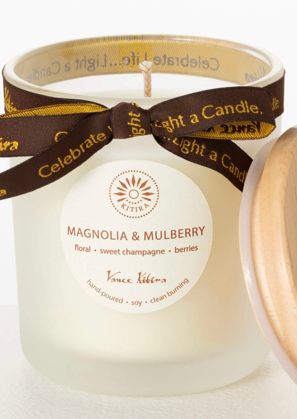 Scented Candle-Magnolia and Mulberry product image features a glass jar, lidded, brown ribbon with gold script, wax, wick, hand-poured, higly scented, clean-burning, paraben-free, all season,  3.5"W x 4"H,  30 hours burn time.