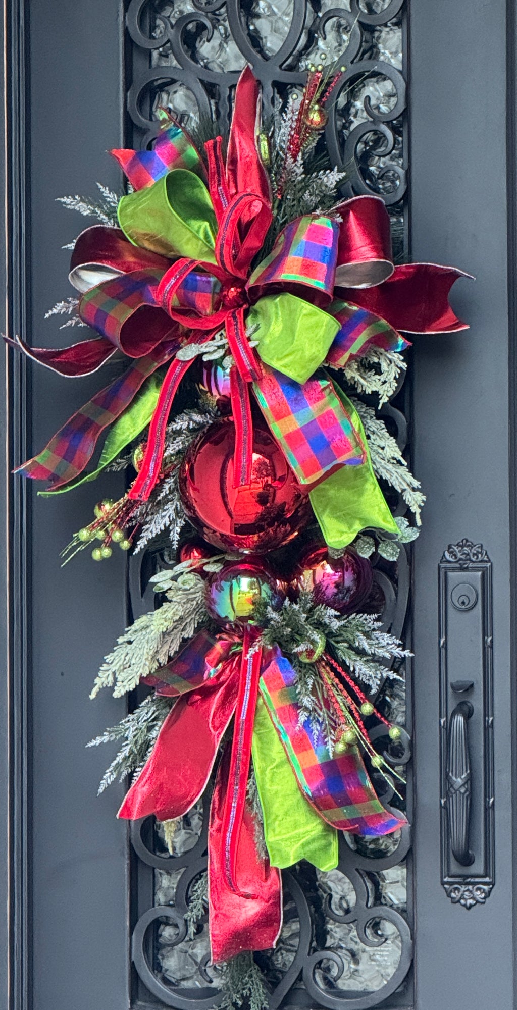 Decorative door swag with red and green ribbons on a door.