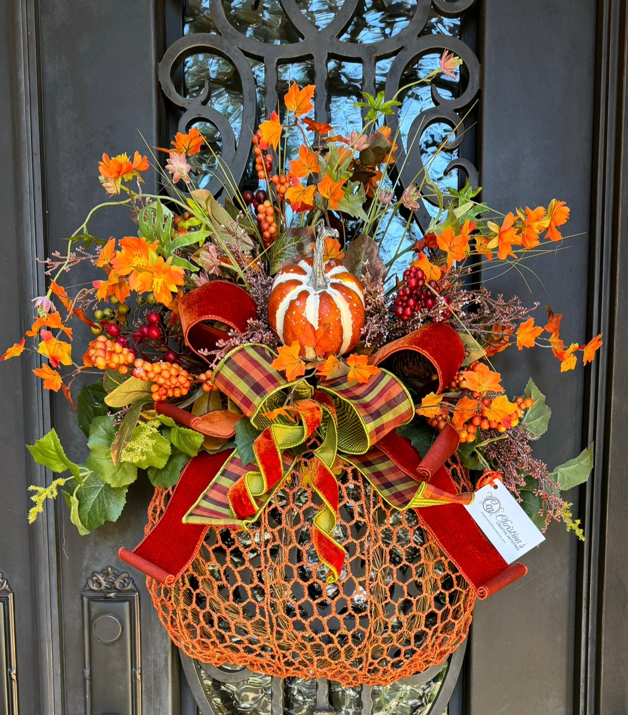 Pumpkin Door Wreath features a pumpkin wreath.   Materials:  grapevine, metal mesh, mixed grenery, faux berries, artificial pumpkin hand tied bow.  Colors:  Burn orange, wine, multicolored plaid .  Measures: 31"H X 29"W.  Comes ready to hang on a nail, hook or wreath hanger.