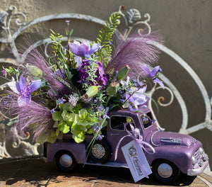 The Color Purple Truck Floral product image features the side view of the flower arrangement and truck planter.  Side view shows the spare tire  and hood that are decorated with rhinestones.  Indoor use or outdoors in a cover porch. Ready to ship.