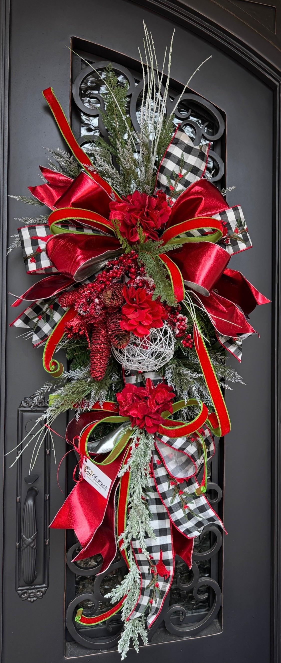 Decorative door swag with red, black and white checkered ribbon with greenery hanging on a door.