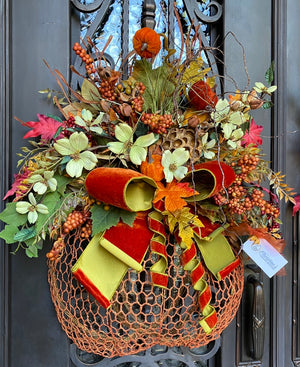 Pumpkin Wreath  product image features fall door wreath.  Half pumpkin frame,  Faux flowers, foam berries, velvet pumpkins, bronzed lotus pod, mixed fall foliage and a large velvet bow.  Colors are shades of orange, green and a hint of deep red.  Materials are grapevine, metal wire, foam, natural pod and velvet.  Measures 30"H X 24" W X 10" Deep.  Indoor/outdoor under a overhang.  Created and Handmade By Christina.  Christina's Creative Artistries Exclusive.   