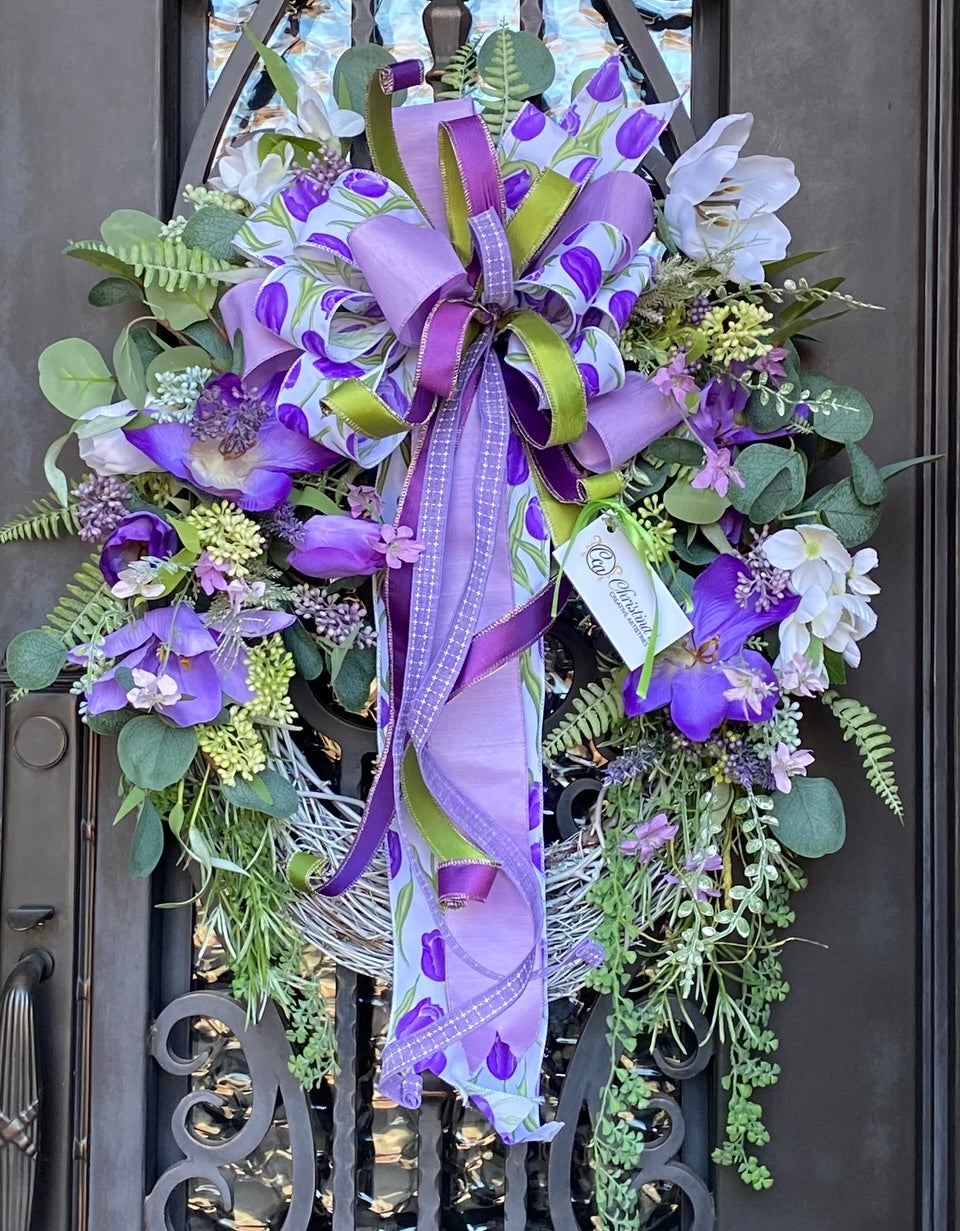 Purple Tulips Wreath product image features purple door wreath.  18-inch, white washed grapevine frame, purple and white tulips, berries and mixed greenery.  Large, multi-layered bow.  Measures 33.5' H x 26" W.  Comes ready to hang on door under an overhang.