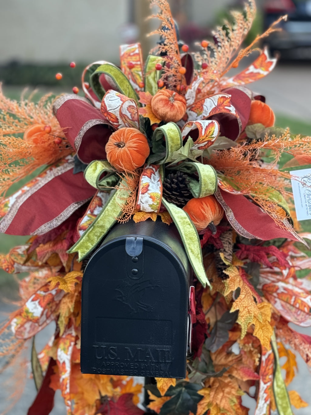 Fall Mailbox Swag product image features a mailbox decoration.  Constructed on pine base.  Maple leaves, pinecones, velvet pumpkins and fern picks accent with three ribbon bow.  Colors are shades of orange, gold and gree.  Materials are polyester, velvet, pvc, foam, natural pinecones.
Measures 45"H x 30"W x 16"L.  Indoor/outdoor use.  Mailbox not included.