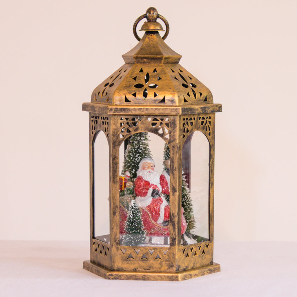 Light Up Brass Lantern features a moroccan shaped brass lantern.  In the lantern sits a resin Santa on a sleigh filled with gifts and two pine trees.  Lights Up.  OnOff switch.  3-AAA batteries required.  Batteries not included.  