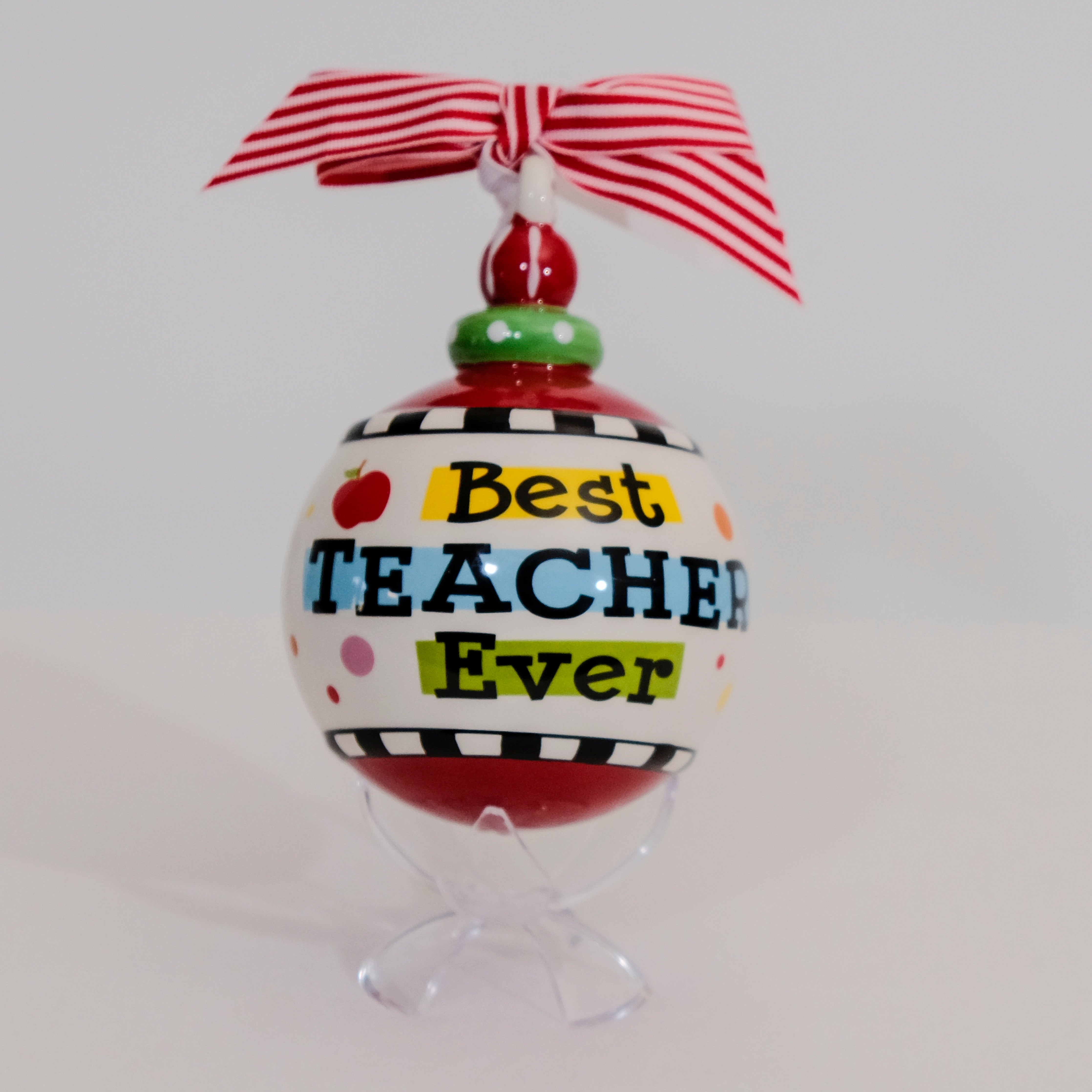 Best Teacher Ever Christmas Ornament product image features, a hand painted ceramic ornament sitting on a clear acrylic stand.  Round with red and white striped bow attached.  Slightly raised lettering in black.  Colors are red, green, yellow and light blue.  Comes with clear acrylic stand.  Hang on tree or sit on acrylic stand.
