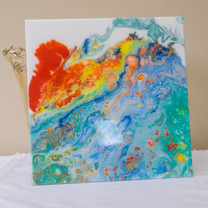 Coral Bay by Christina Russell.  Features acrylic painting in blues, orange, yellow, teal and white on 12 inch by 12 inch glass.  Resin finish. Modern/ Contemporary.  Can be framed or mounted.