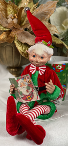 Reading Christmas Elf product image features a Christmas elf reading a Santa book.  16 inches tall .  Dressed in red, green and peppermint stripes.  Posable with bendable arms and legs.  Decorative accessory.  Collectible.  Not a toy for children.  