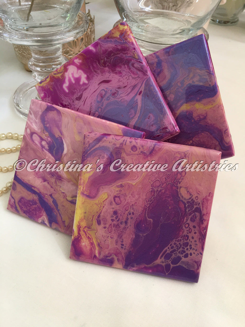 Shades of Purple Coasters product image features a set of 4" x 4" ceramic coasters.  Hand painted.  Abstract with a pearly luster in shades of purple and yellow.  Each coaster  has its own unique design.   Cork-backed.  Durable finish.   1  acrylic coaster stand.  Beautiful.  Unique coasters.   Protect your table surfaces while enjoying a nice cold drink.  Wipe your coasters off with a clean damp cloth.     