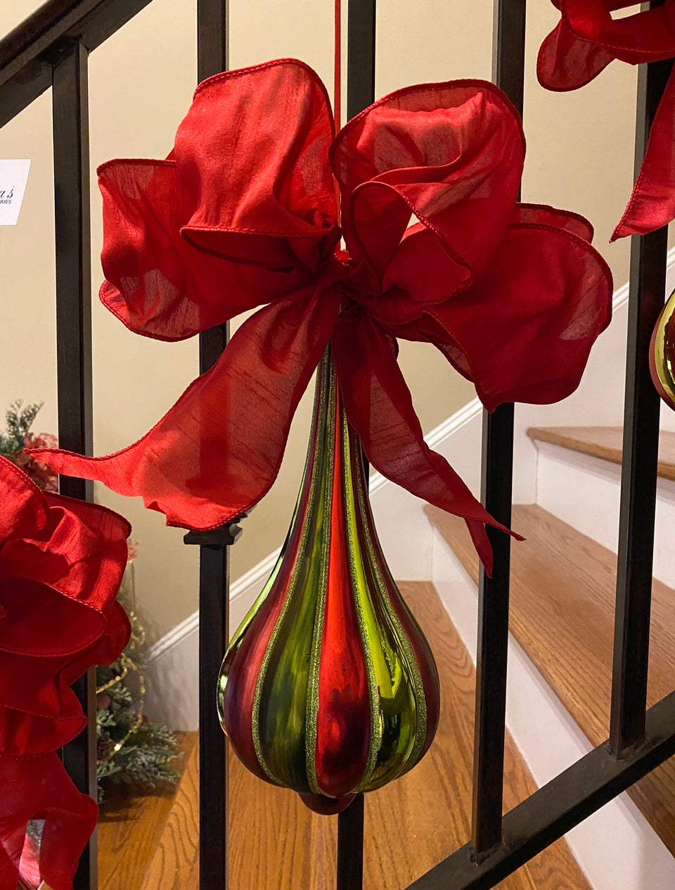 Red Green Teardrop Ornament With Bow product image features  a Christmas ornament.  Red and green color.  Red bow atop ornament.  Red ribbon hanger.  Ornament alone is 13.5" long.  Measures 26" L x 9.75" W across bow.  Best for indoors or outdoors under a covering.