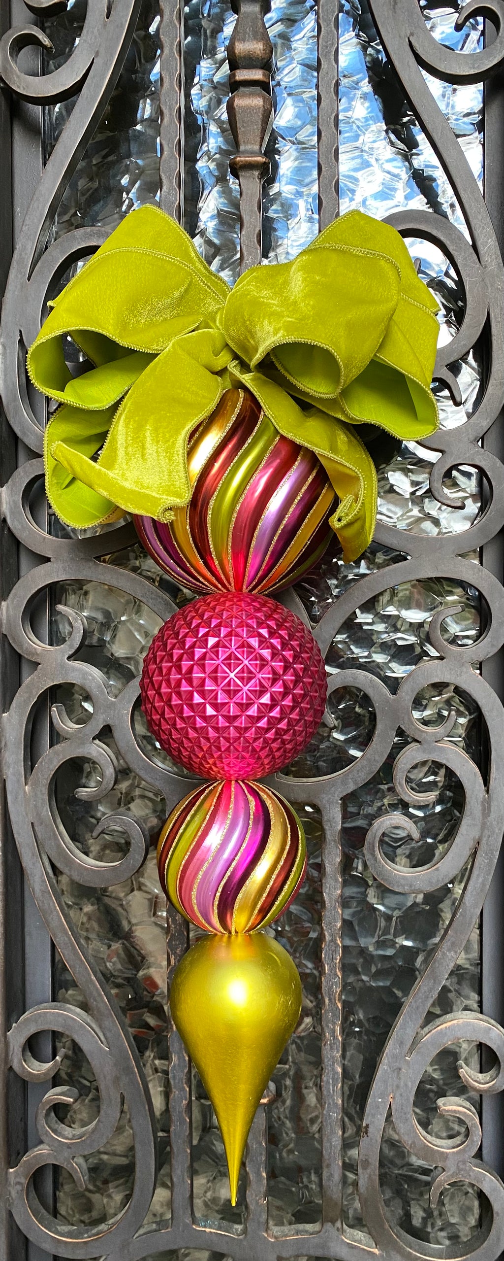 Large Christmas Ornament With Bow product image features a multi colored finial ornament with a bow.  Shatterproof ornament.  Hand tied bow in chartreuse color.  Ornament has three round balls in graduating sizes...largest at the top to a tear drop at the bottom.  Colors are chartreuse, hot pink, purple, lavender and gold.  Ornament measures 21.75"L X 5.5" W .  With Bow, Ornament measures 26"L X 11" W.  Best used indoors or in a covered area.  Shatterproof ornaments can still break so handle with care.