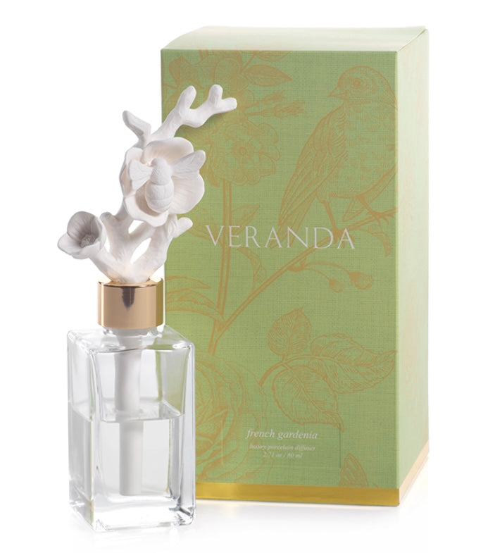 Zodax Veranda Bee On Flower Porcelain Diffuser product image features a clear glass bottle filled with 80 ml of french gardenia oil fragrance.   One porcelain bee perched on a porcelain flower diffuser insert.  Fragrance disperses through the porcelain bee on flower diffuser.   Diffuser is 7" tall. Gift box is 8.5" tall x 4.25 " W. Allow 24-36 hours for full fragrance effect. Fragrance refills available in store.