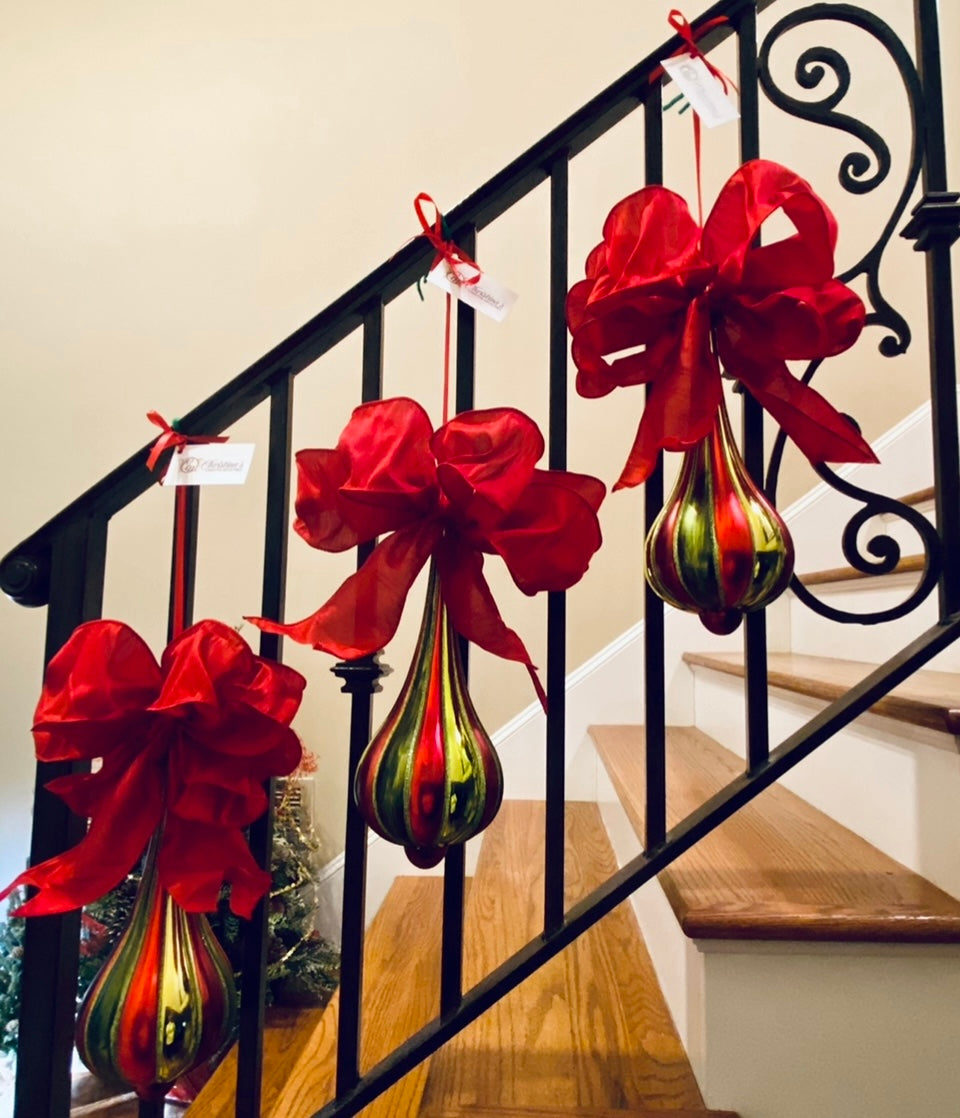 Red Green Teardrop Ornament With Bow product image features  three red and green Christmas ornaments hanging  side by side on a staircase railing.