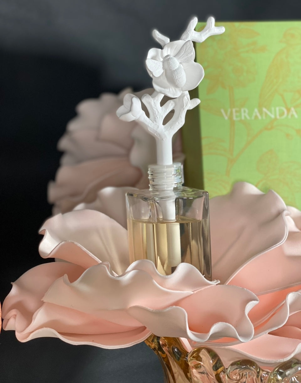 Zodax Veranda Bee On Flower Porcelain Diffuser product image features a sealed, clear glass bottle pre-filled with 80 ml of french gardenia oil fragrance.   One bee perched on a porcelain flower diffuser.   Fragrance disperses through the porcelain bee on flower and twig diffuser.  Bottle dimension is 3.25"X 7.5".  Allow 24-36 hours for full fragrance effect. Fragrance refills available in store.