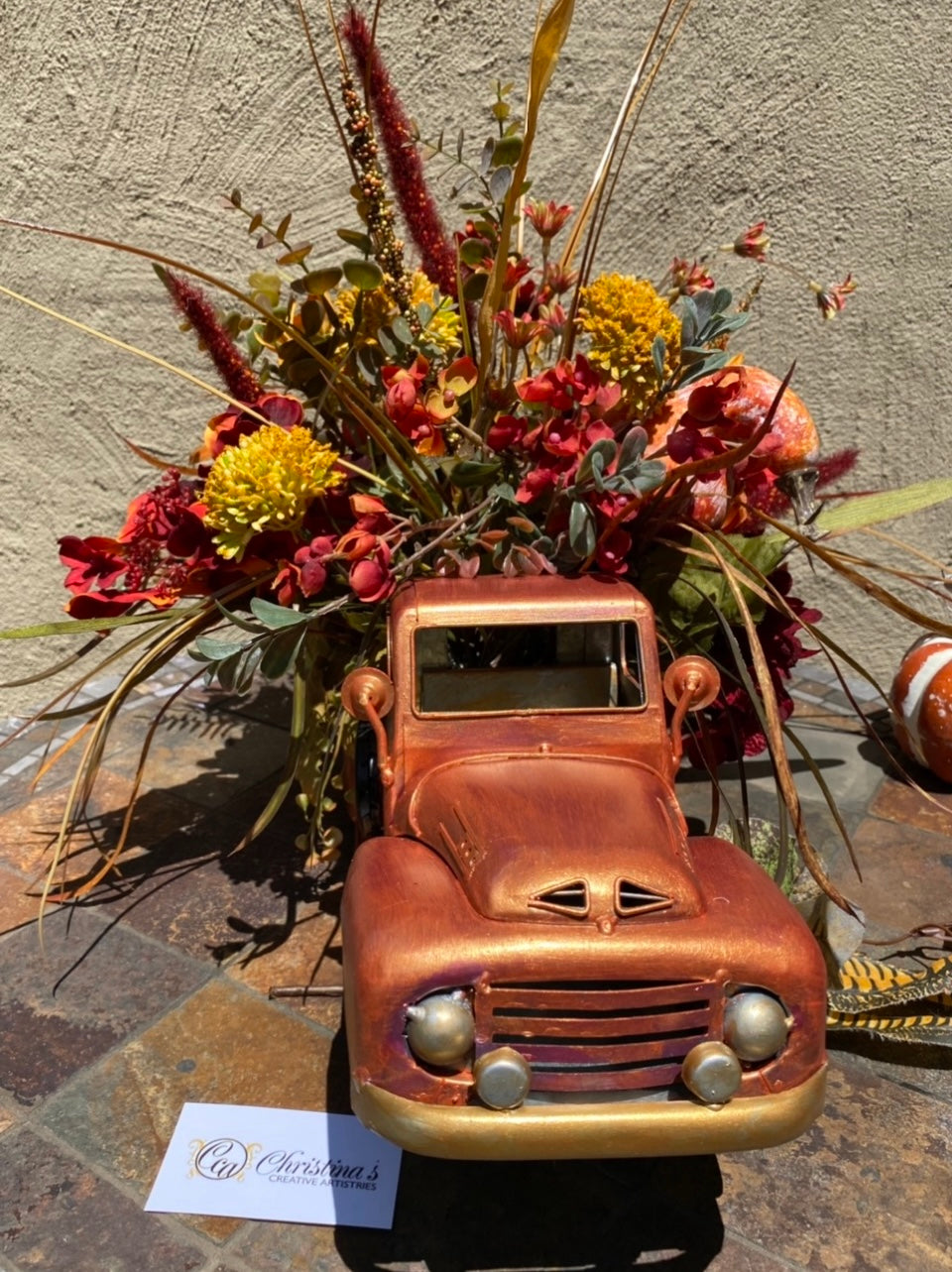 Orange 1948 Chevy truck planter filled with faux fall flowers.  Faux floral arrangement. Indoor decorative use.  