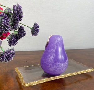 Timber Pear Candle Wisteria product image features one pear shaped candle.on a gold rimmed glass tray. Vance Kitira Collection.  Color is wisteria. This candle burns clean , smokeless, unscented, environmentally-friendly and boast long burn time. Measures 3"L X 4.5"H. Gold rimmed glass trays available for purchase in store.